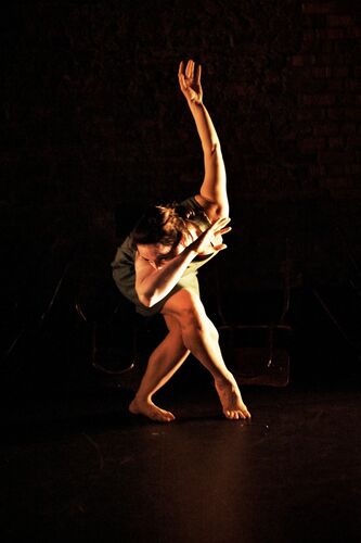 A figure in movement with one arm bent and the other stretched upwards behind