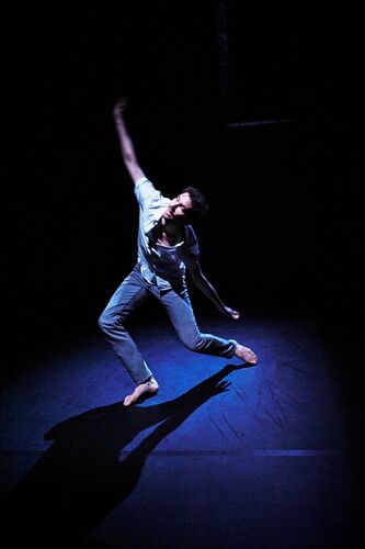 A figure in movement cast in blue light on stage