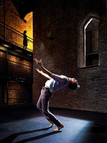 A figure in a back bend spotlit on stage