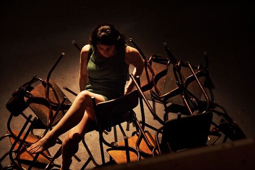 A figure sitting surrounded by upturned chairs