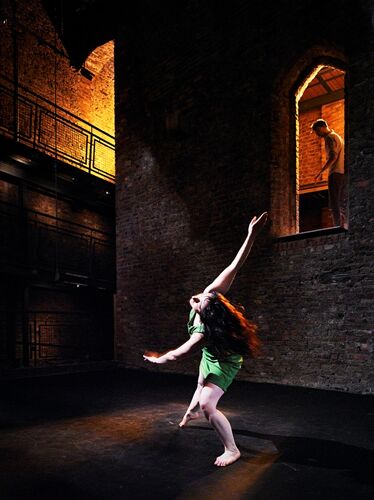 A figure in movement spotlit with a further figure watching from above