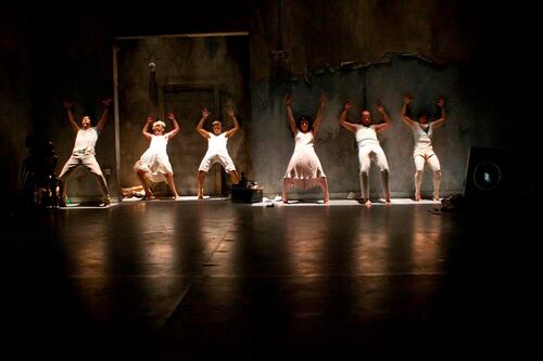 Six figures in a line leaning back against a wall cast in light from above