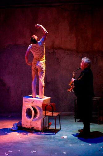 A figure standing in movement on top of a washing machine with another figure playing saxophone