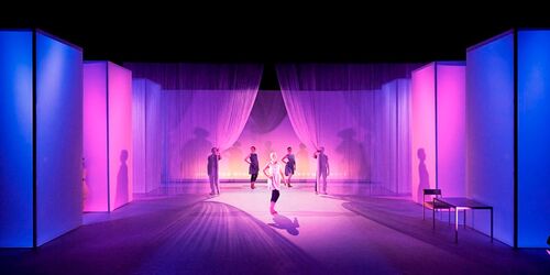 Five figures standing spread across a stage lit in pink and blue