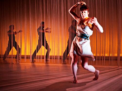 A figure in movement in front of a fringe curtain with three figures behind it