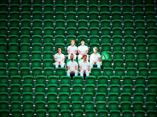 Six figures dressed in white seated in the middle of a large bank of green stadium seats