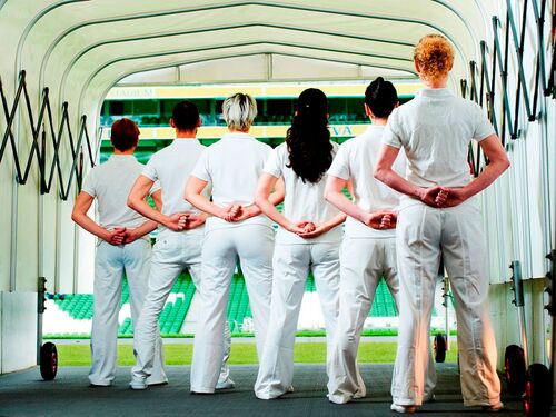 Six figures dressed in white seen from behind in the tunnel leading on to a sports pitch