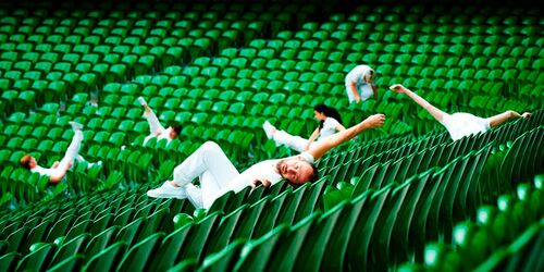 Six figures dressed in white in movement scattered across a stadium bank of green seats