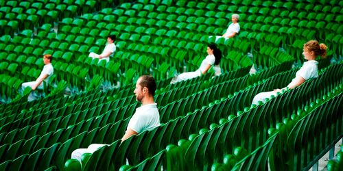 Six figures dressed in white sitting scattered across a stadium bank of green seats