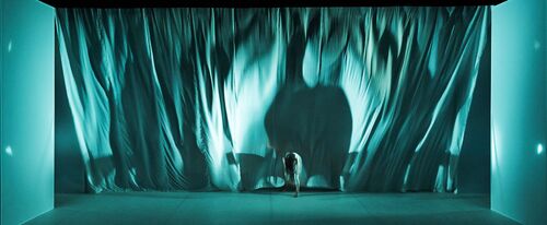 A turquoise lit stage with a figure in movement at the centre