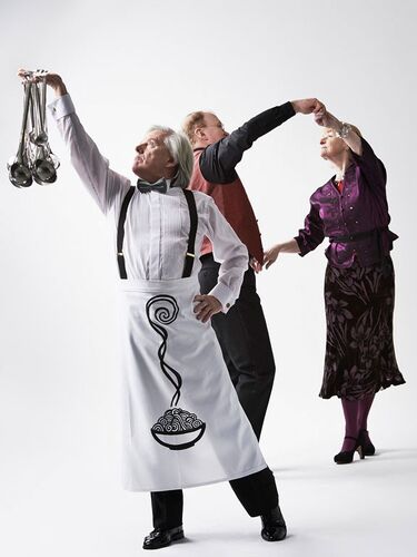 A figure in an apron holding many ladles while two others dance together in the background