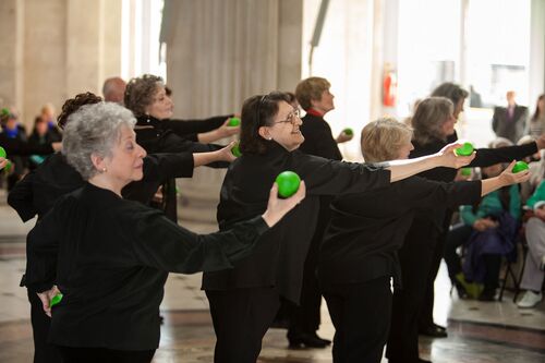 An ensemble of participants holding green apples in outstretched hands