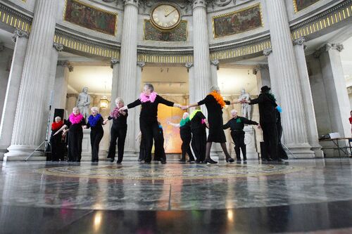 Participants in movement in the centre of City Hall with brightly coloured boas around their necks