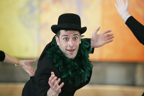 A figure with a dark feather boa around his neck and bowler hat in movement