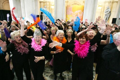 Participants posing and waving to camera with colourful feathers inside City Hall