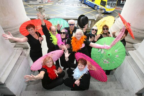 Participants posing on the steps of City Hall with brightly coloured parasols and feathers