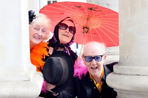 Three participants posing outside City Hall with sunglasses, coloured feathers and a parasol
