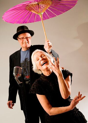 Two participants posing in a studio with a pink parasol and old fashioned microphone