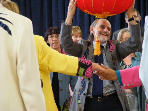 A participant laughing and holding a red lantern above his head with others in movement around him