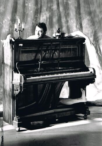 A man's head and an assortment of limbs emerging from the body of a piano