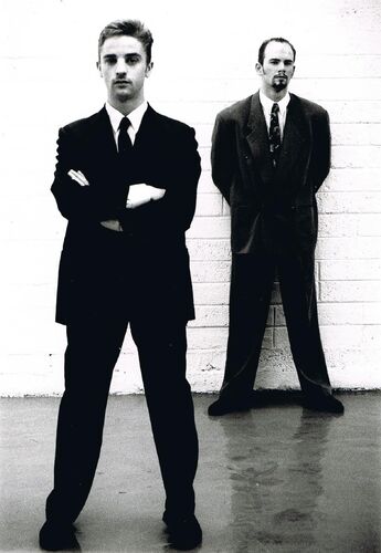 Two figures in suits standing in black and white
