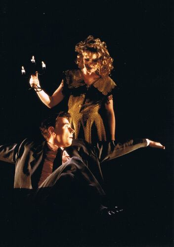 One figure seated with legs crossed with another standing behind him holding a candelabra