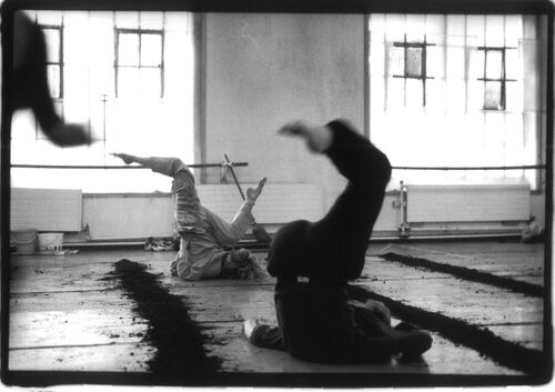 Two figures in movement on the floor with legs raised upwards