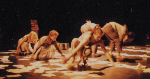 Five figures in movement on a stage littered with sheets of paper