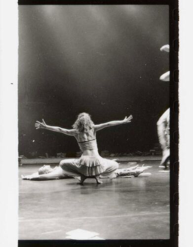 A figure with their back to camera in a crouch on the floor with arms spread wide