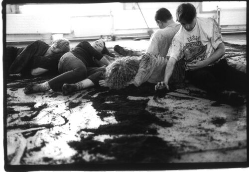 An ensemble of dancers in movement on the floor surrounded with soil