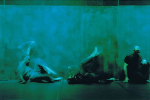 Three figures blurred in motion against a wall cast in green light