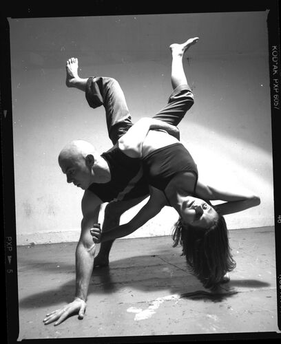 Two figures in movement together with one held upside down mid-lift by the other
