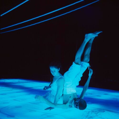 One figure seated on the stage floor with another in movement against her with legs raised