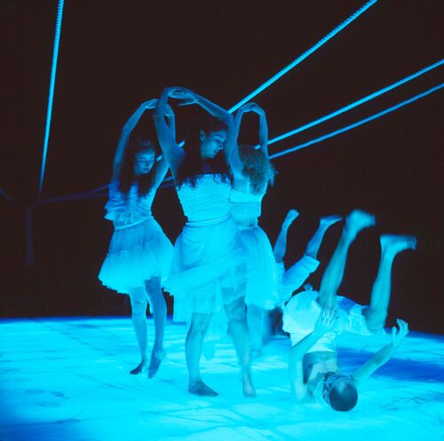Three figures in movement standing and two figures on the floor all cast in blue light