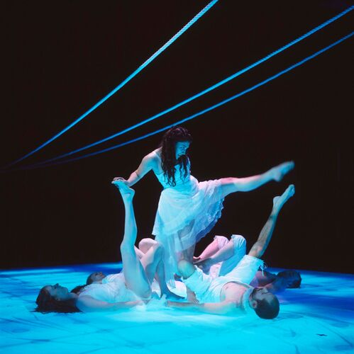 A figure in movement at the centre of a cluster of other dancers upraised legs