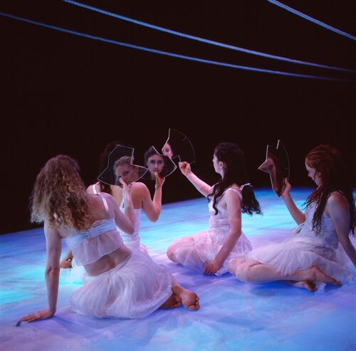 Four figures seated on the stage floor holding shards of mirror in front of their faces