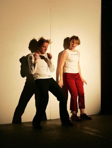 Two figures in movement against a blank white wall