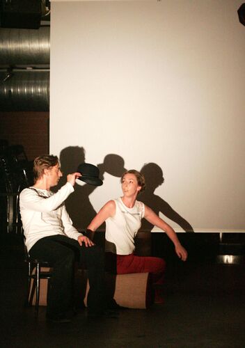 Two figures seated by a blank wall with shadows being cast behind them