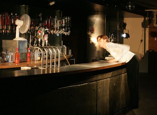 A figure in movement leaning over the counter of a bar