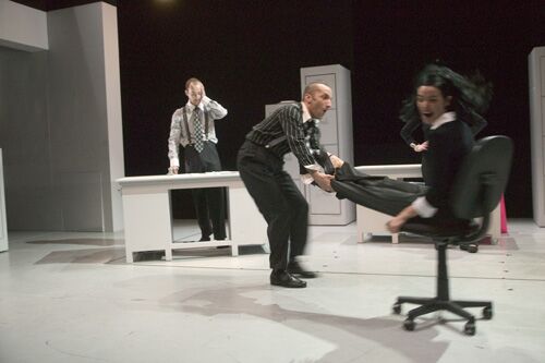 One figure swinging another around the stage on an office chair and another standing at a desk