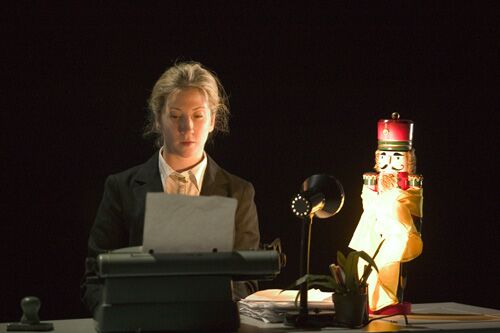 A figure sitting at a desk with a nutcracker doll on the desktop beside her