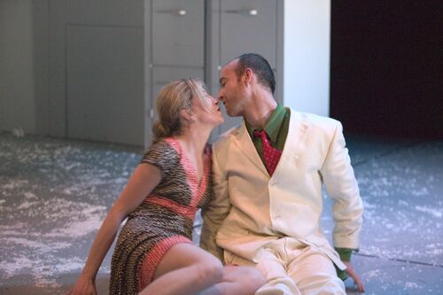 Two figures near kissing seated on the stage floor