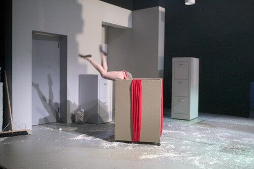 A pair of bare legs emerging, waving from a large box in an office set