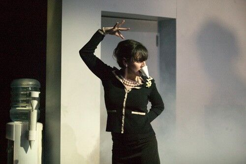 A figure in a skirt suit in movement with a water cooler cup held in her teeth