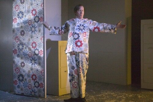 A figure in matching top and bottoms in the same pattern as the wall beside him