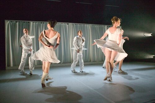 An ensemble of dancers in movement dressed all in white on a white stage