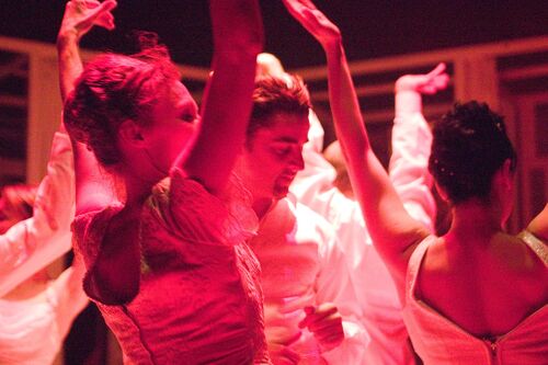 An ensemble of figures cast in pink light in movement