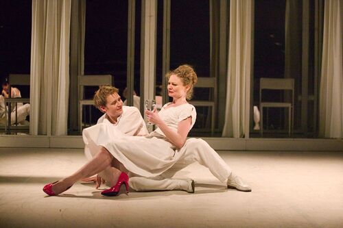 Two figures seated on the stage floor with one seated in the others lap