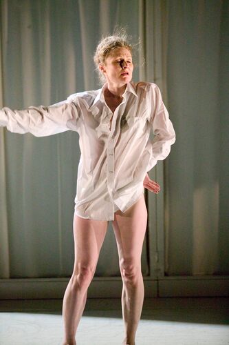 A figure in a white shirt with bare legs in movement on stage