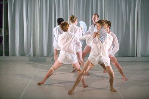 Six figures in white shirts with bare legs in movement on stage